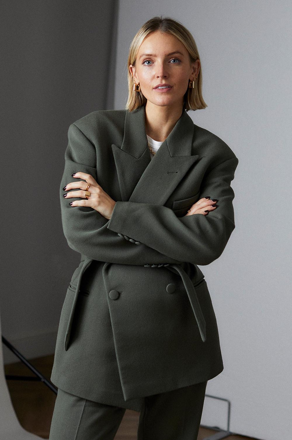 Person wearing an olive green oversized blazer with arms crossed, paired with matching trousers.