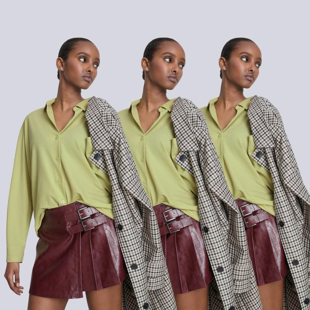 Model wearing lime green shirt, burgundy leather mini skirt with buckle detail and checked coat draped over shoulder.