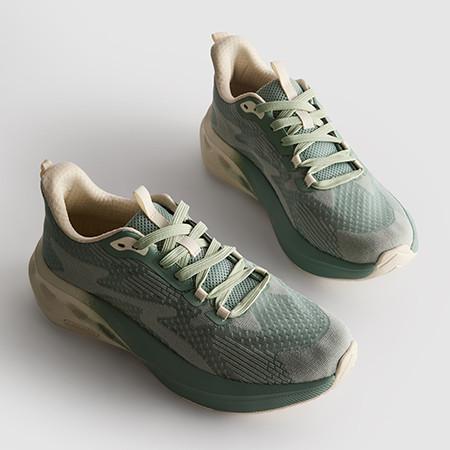 Pair of sage green trainers with beige laces and cushioned soles in a textured mesh material.