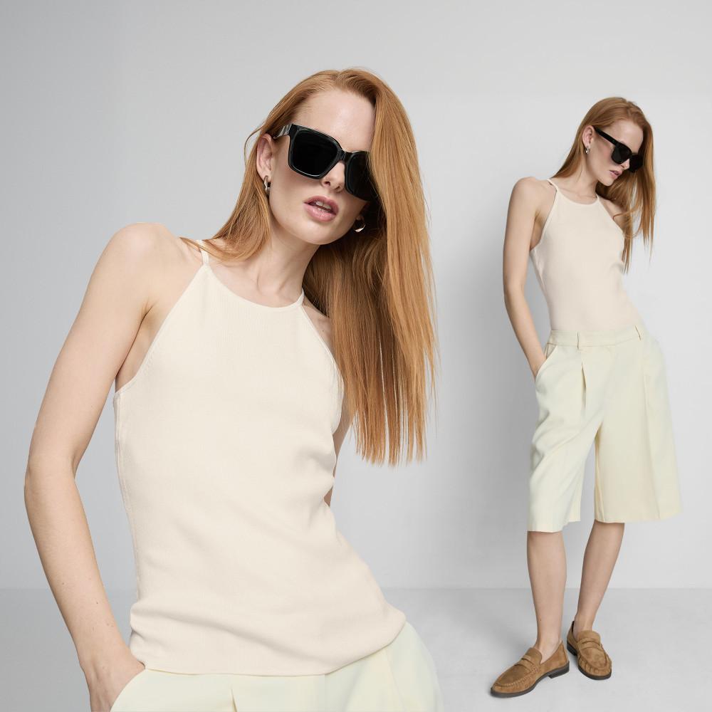 Model wearing cream halter neck top, tailored shorts and black sunglasses with brown loafers.