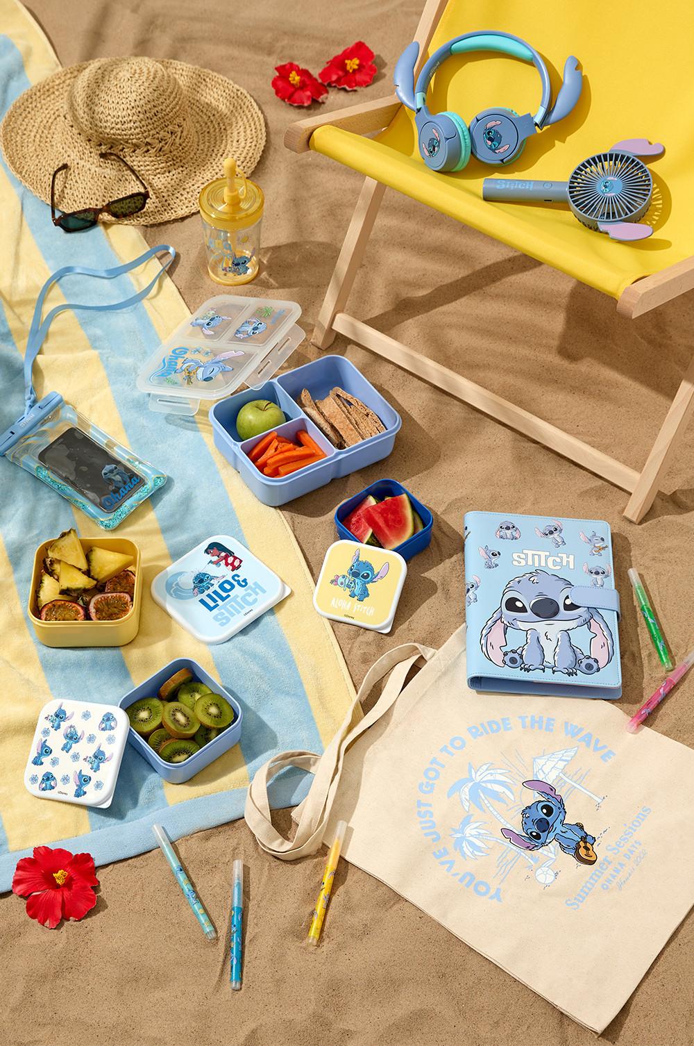 Stitch merch displayed on a beach set including cup with a straw, lunchboxes, notebook, tote bag, headphones, colouring pens and handheld fan