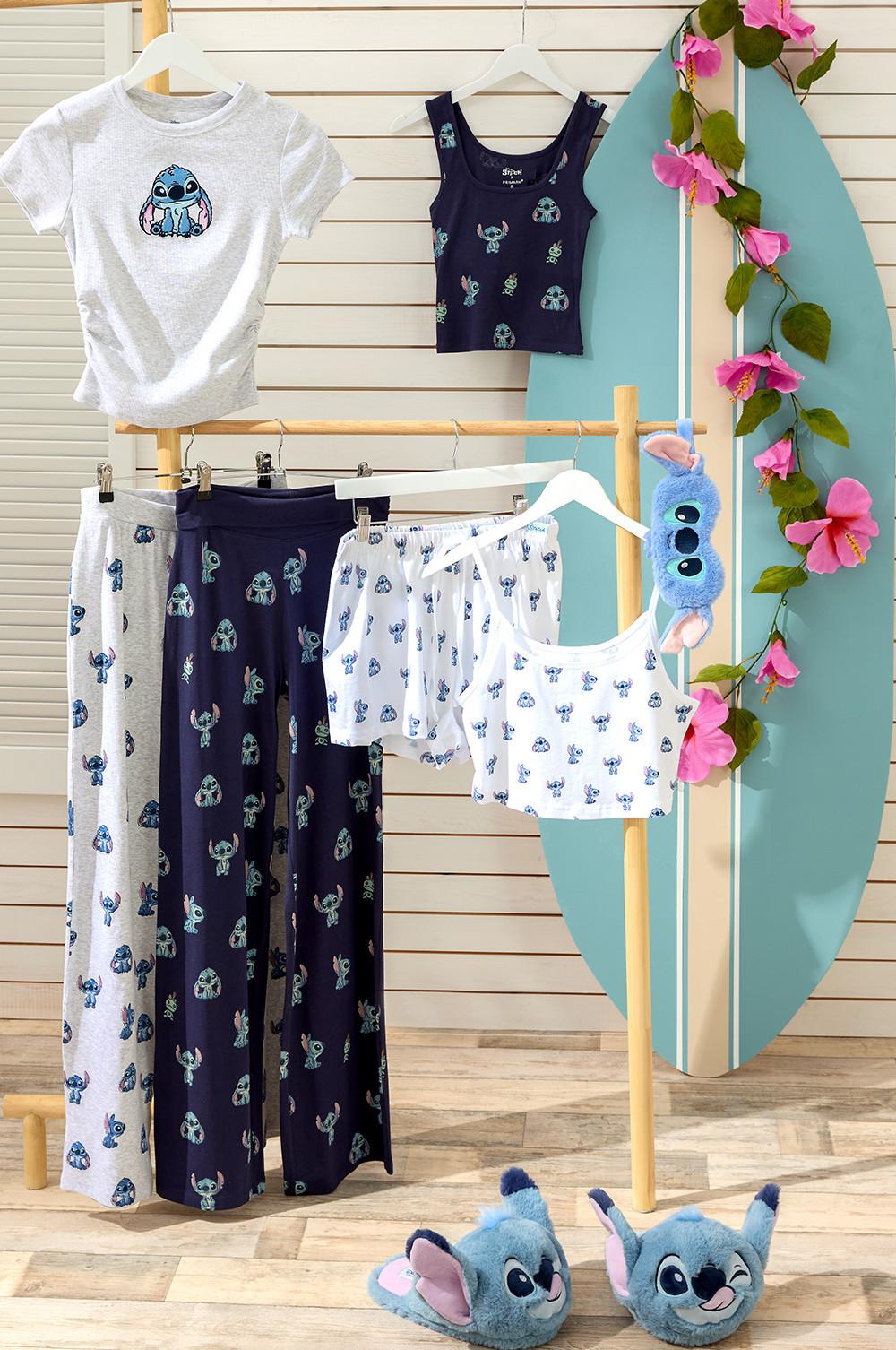 Stitch nightwear collection on hangers showcasing a short sleeved white graphic top, matching black and white pyjamas set, eyemask and stitch slippers.