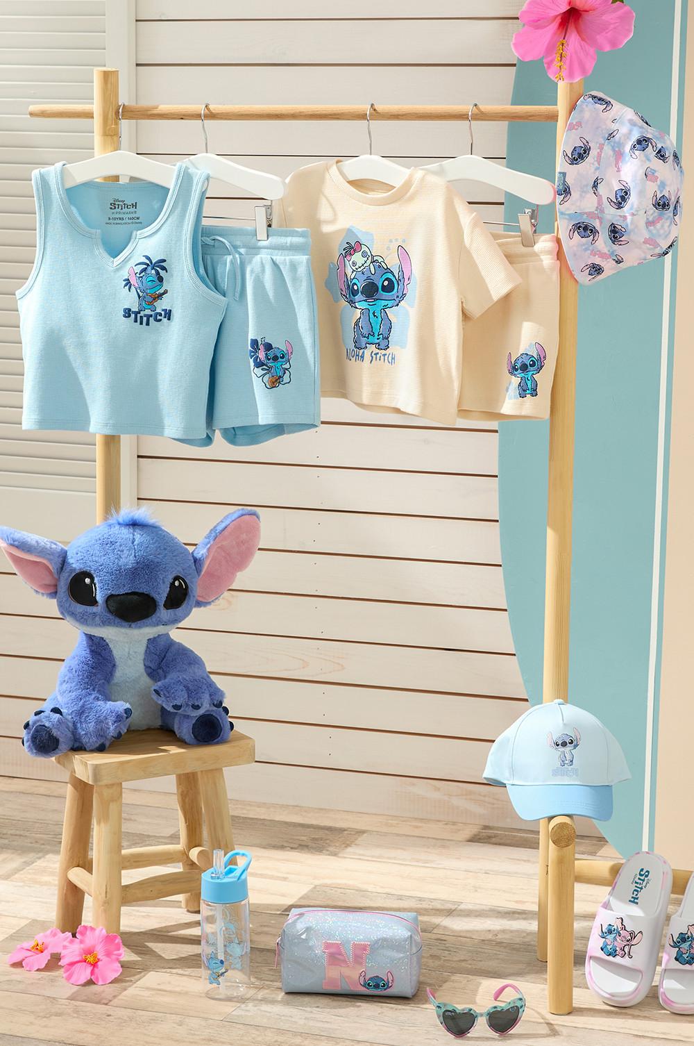Stitch clothings on hangers showcasing matching tops with shorts in pale blue and pale yellow. Including a stitch plush toy and accessories such as water bottle, small bag, sunglasses, baseball cap, sliders and bucket hat.