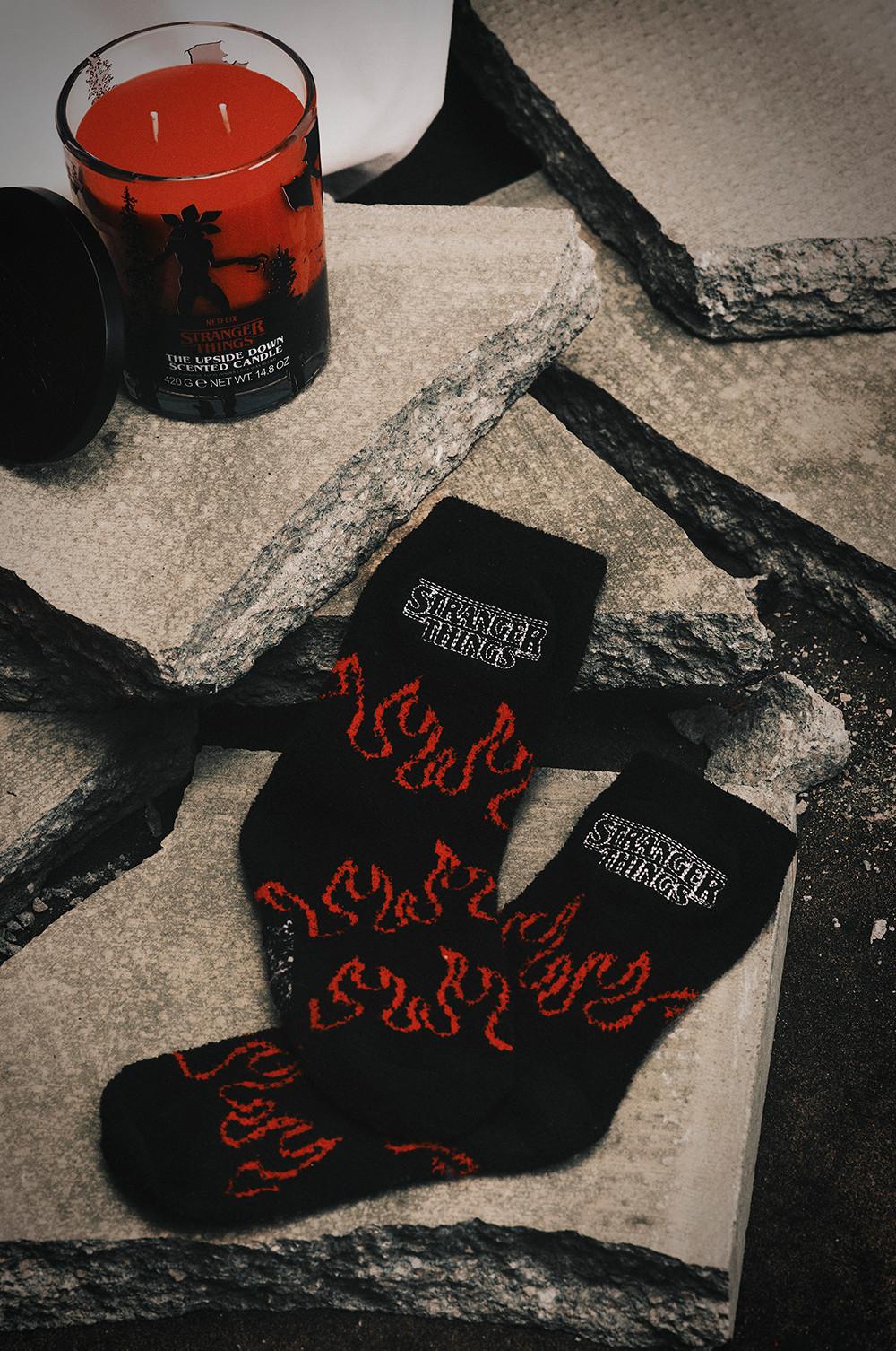 Stranger Things black socks with red flame pattern and a matching scented candle on stone surface.