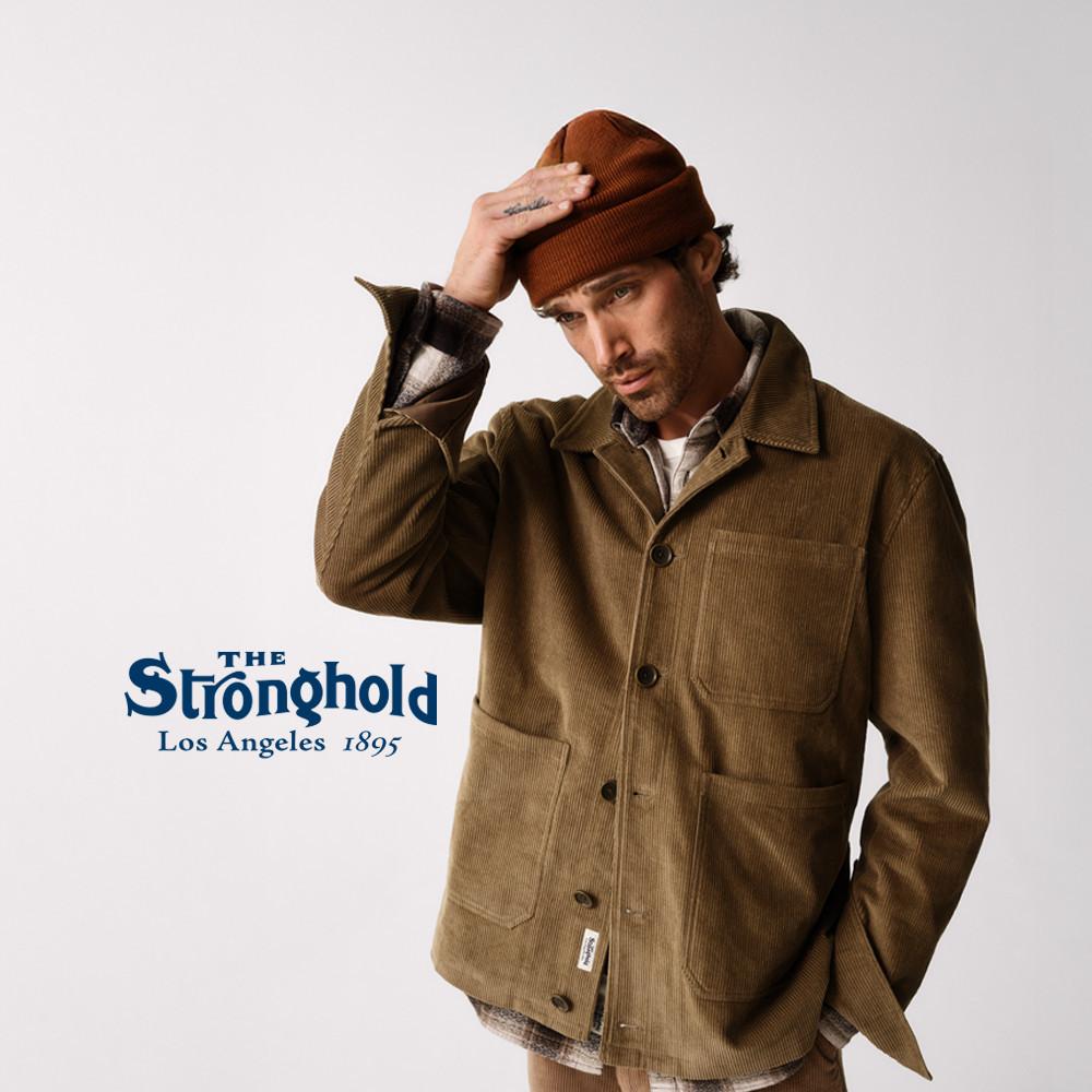 Person wearing brown corduroy jacket and rust beanie from The Stronghold clothing brand.