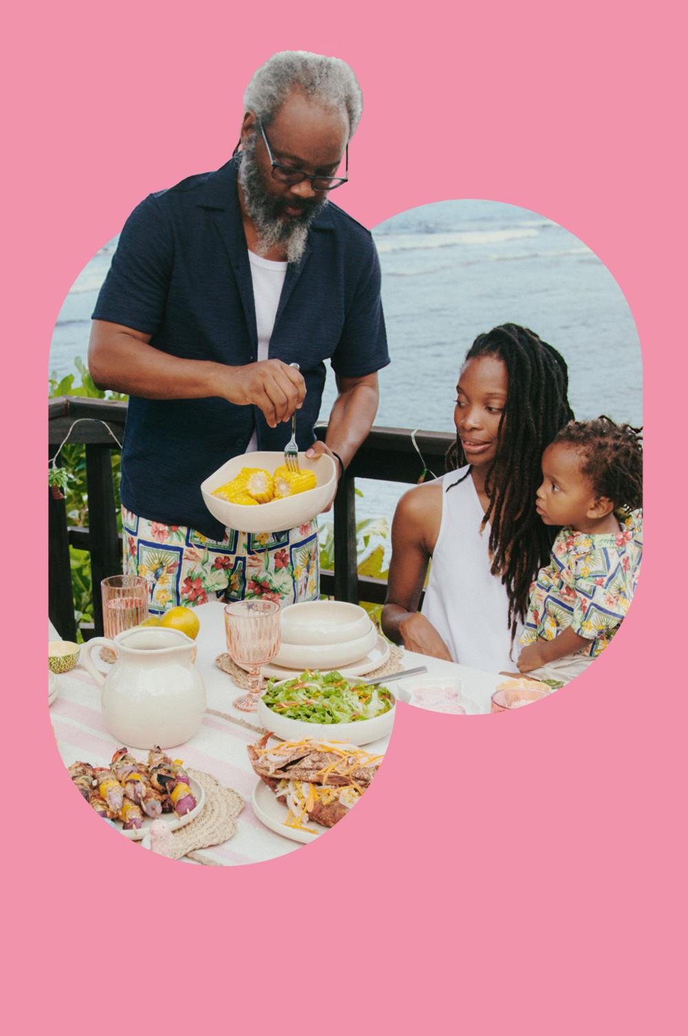 Famille dînant en plein air avec de la vaisselle blanche, un verre rose et des sets de table tressés