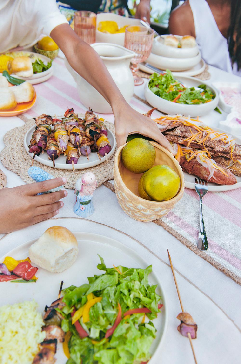 La table est dressée avec des grillades sur des assiettes blanches, y compris des sets de table tressés, une salière et une poivrière en forme de perroquet et un bol en forme d'ananas.