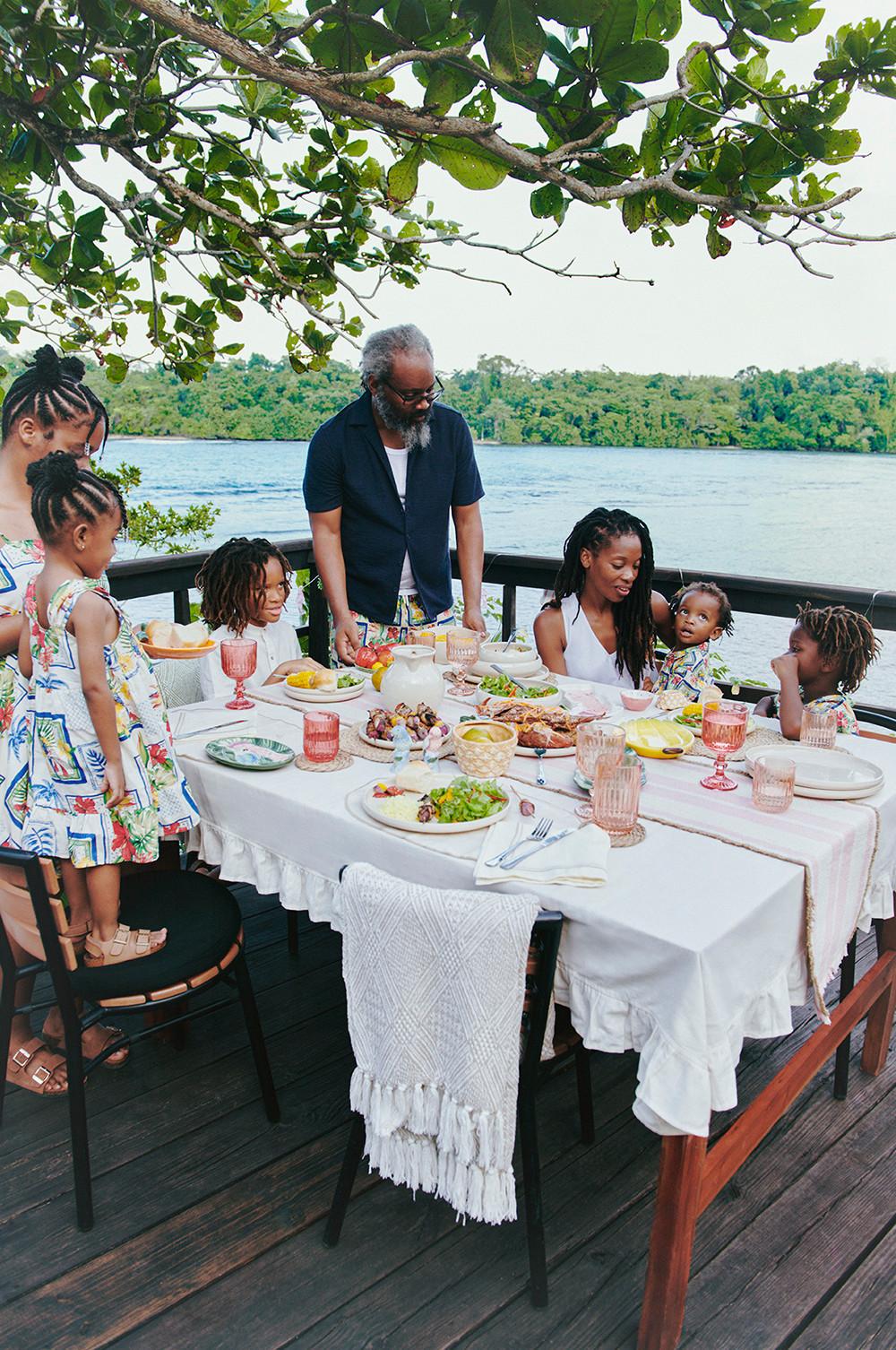 Famille réunie autour d'une table en plein air avec des grillades et de la vaisselle à motif tropical.