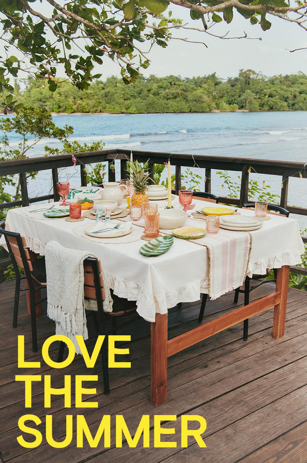 Outdoor table with white tableware, pink drinking glass, fruit shaped dishes and woven placemats