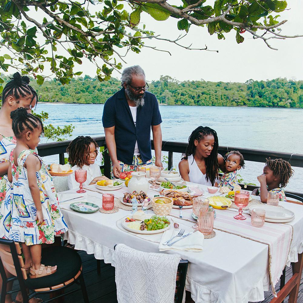 Famille autour d'une table dînant à l'extérieur avec des bols blancs et de la vaisselle en céramique à motif tropical.