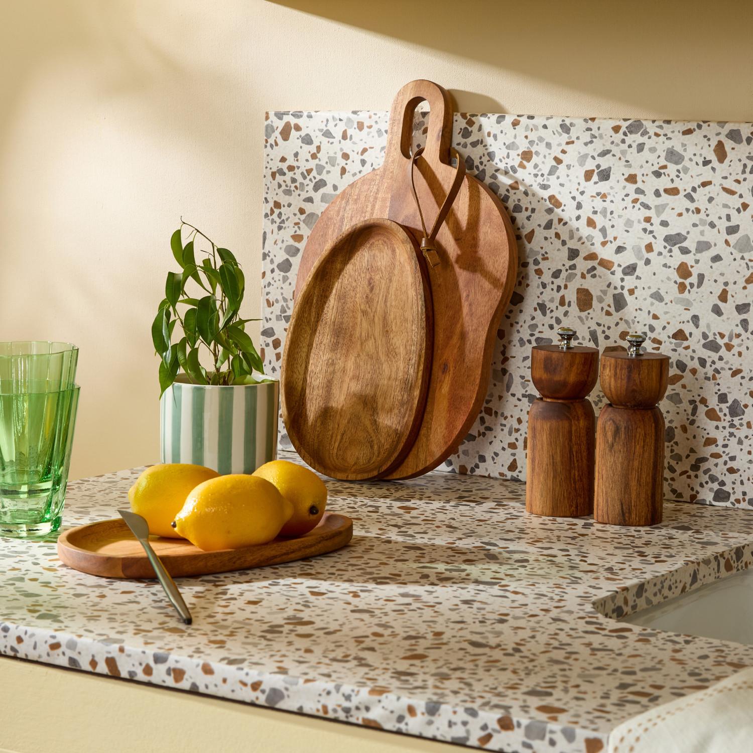 Stylish kitchen with terrazzo worktop featuring wooden chopping boards, lemons, salt and pepper mills, and a small plant.
