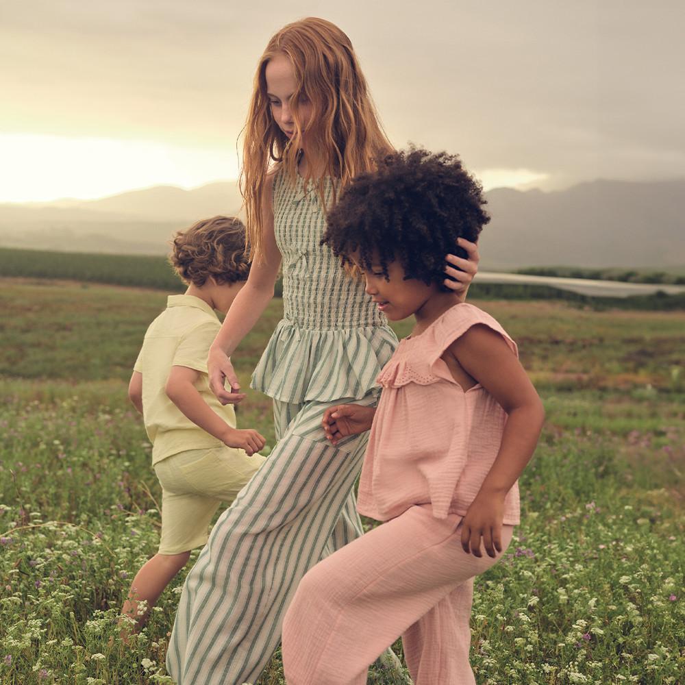 Three children wearing various pink, blue and yellow summer top and pants sets