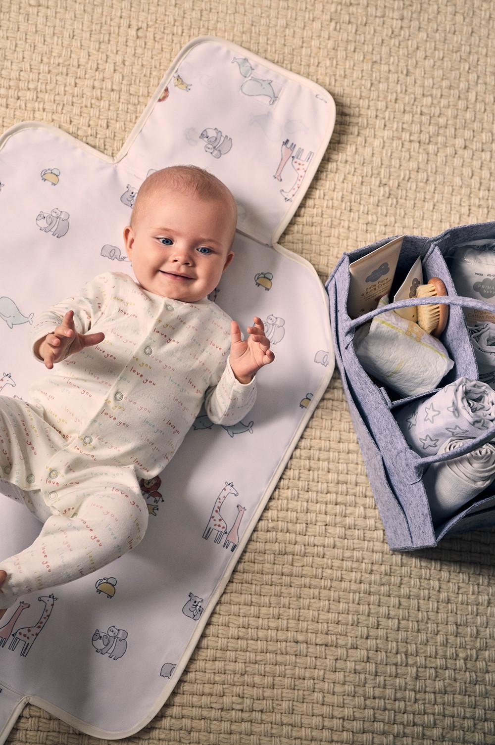 Bebè sdraiato su un materassino con accessori per neonato, foto intera