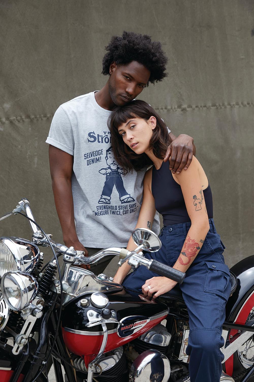 Models tragen Jeans und Oberteile auf/hinter einem Motorrad