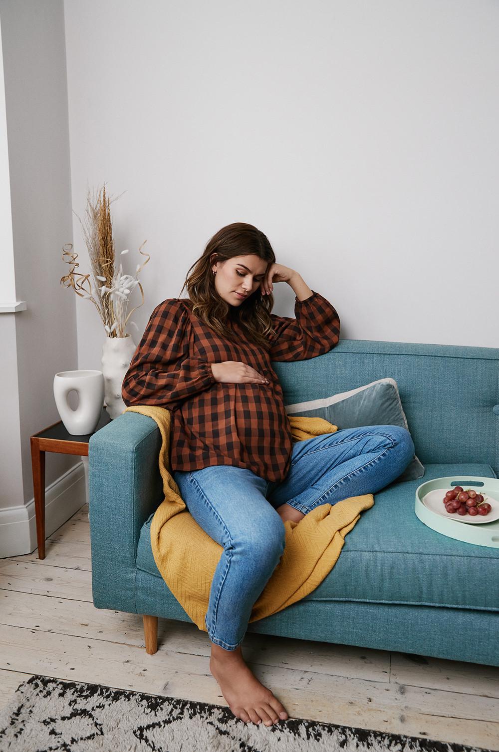 modella sul divano con maglietta e jeans che guarda il suo pancione