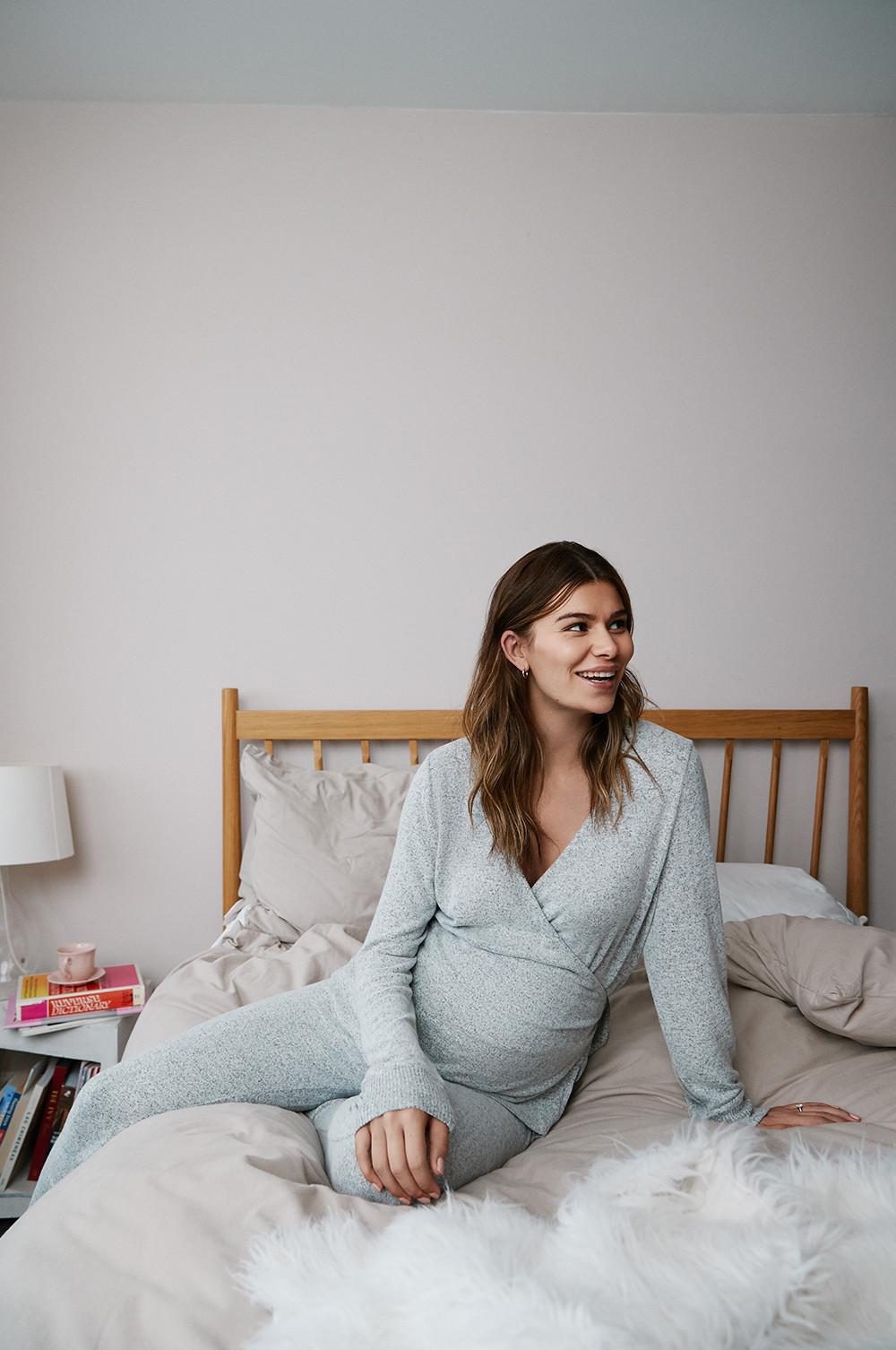 modelo sentada en la cama y sonriendo con un conjunto cruzado gris