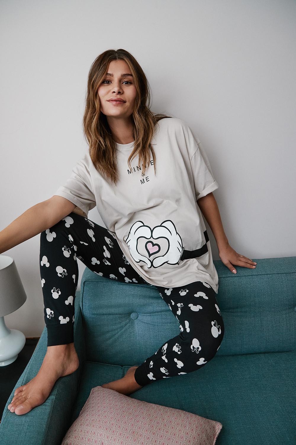 model sits on teal coloured sofa, wearing grey minnie mouse pyjamas