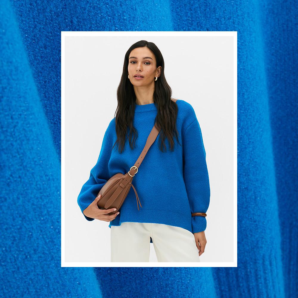 Bright blue knitted sweater with relaxed fit, paired with white trousers and brown leather crossbody bag.
