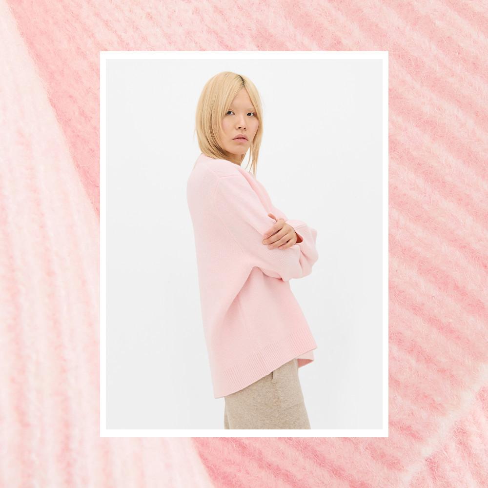 Person wearing a soft pink oversized sweater with beige bottoms, standing with arms crossed.