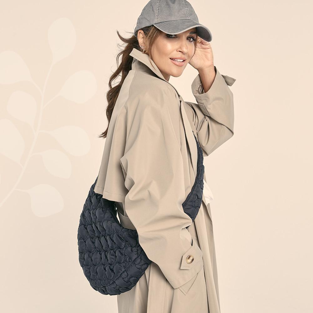 Paula Eche porte un trench, un sac à bandoulière gris et une casquette en denim gris