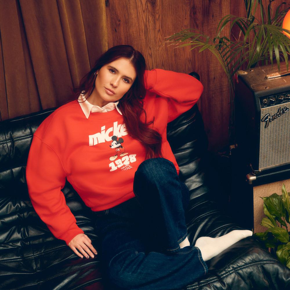 Mimi Webb wearing bright red Mickey Mouse sweatshirt with white collar and blue jeans