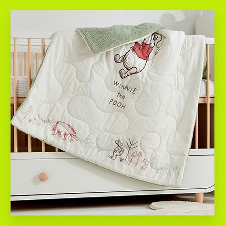 Childs nursery blanket with Winnie The Pooh design, hanging over a crib