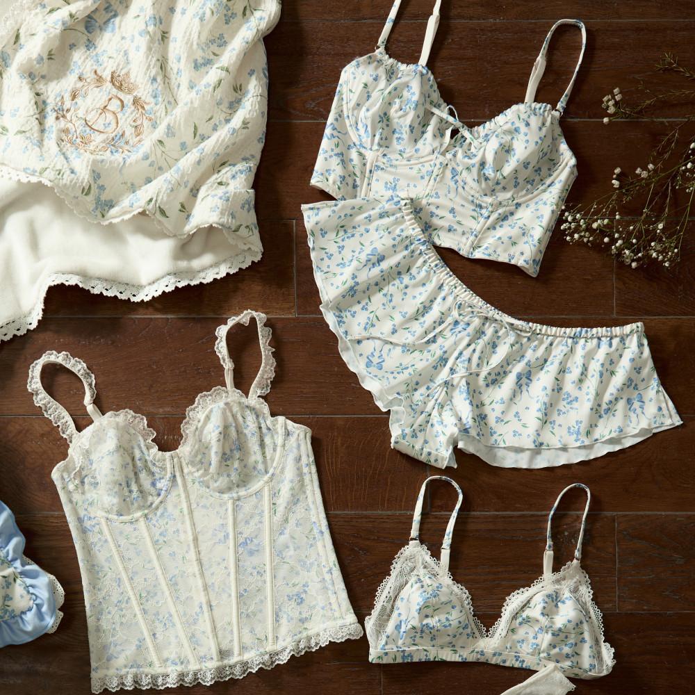 Collection of feminine lingerie with blue floral pattern including corset, bralettes and shorts on wooden surface.