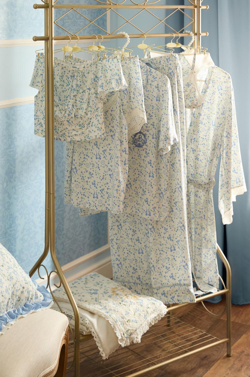 Floral patterned pajama set in blue and cream hanging on a gold clothing rack with matching folded items below.