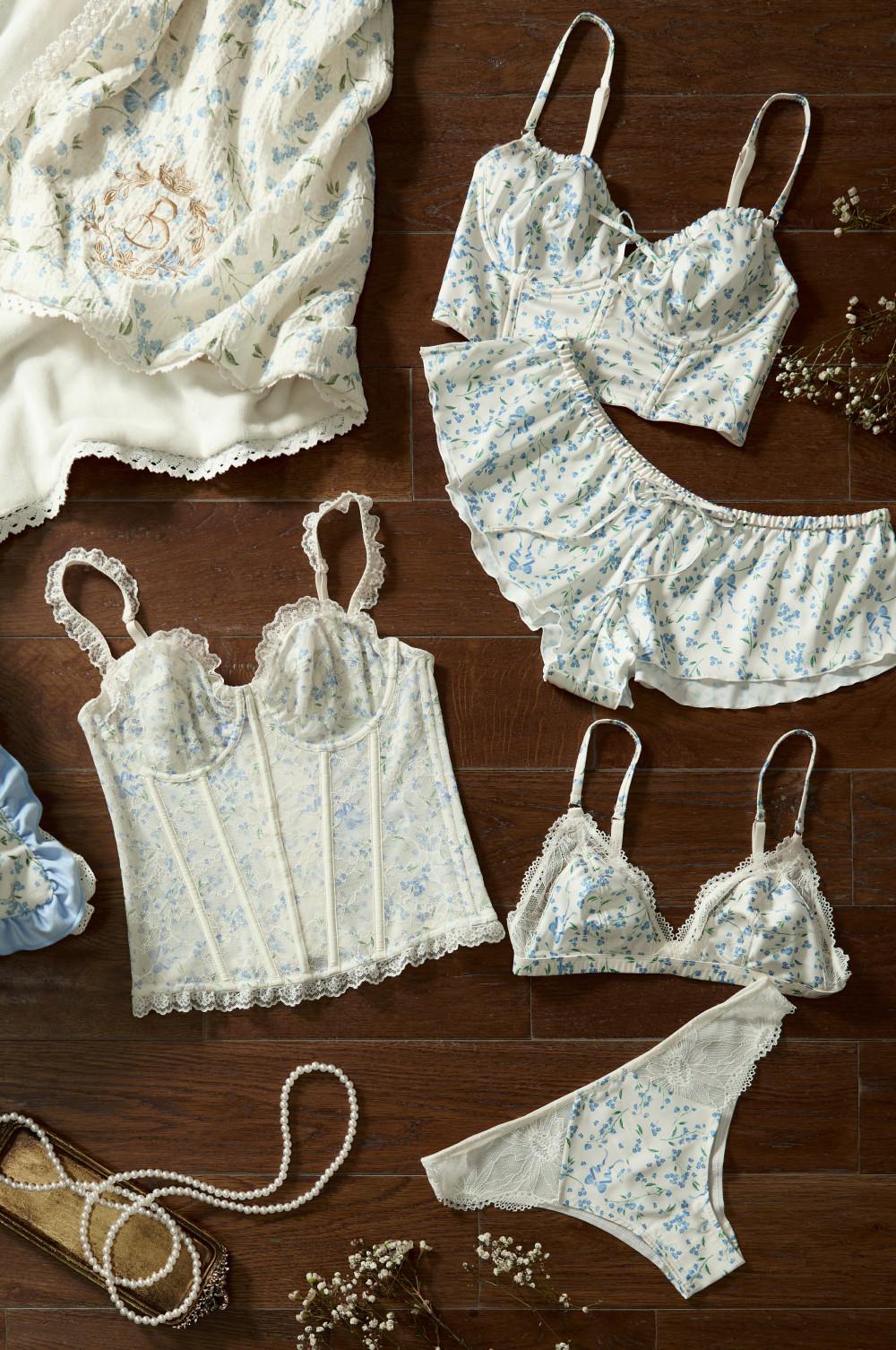 Collection of cream and blue floral lingerie including corset, bralettes, shorts and briefs on wooden surface.