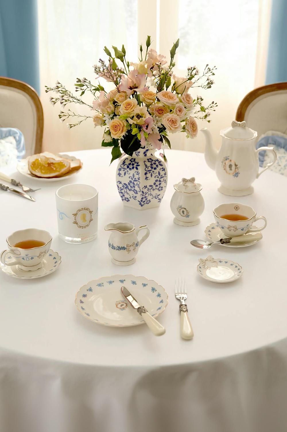 Elegant tea set with porcelain cups, teapot and blue-patterned dishes around a floral centerpiece in a vase.