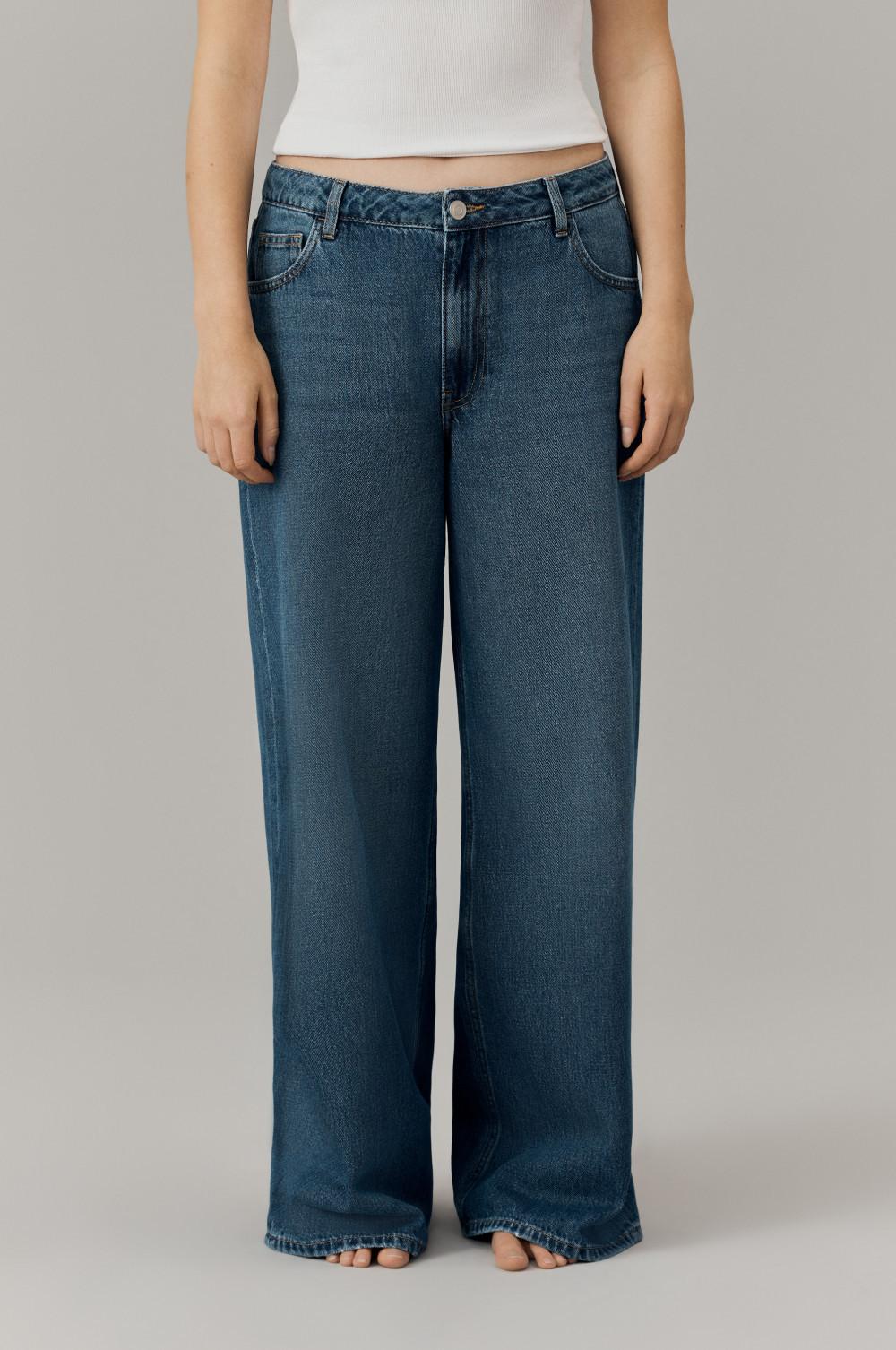 Person wearing wide-leg blue denim jeans with a cropped white top against neutral background.