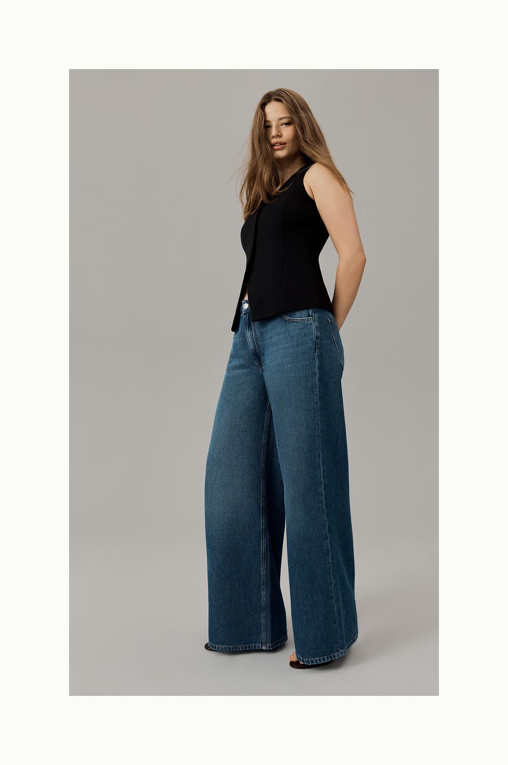Person wearing black sleeveless top with side slits paired with wide-leg blue denim jeans.