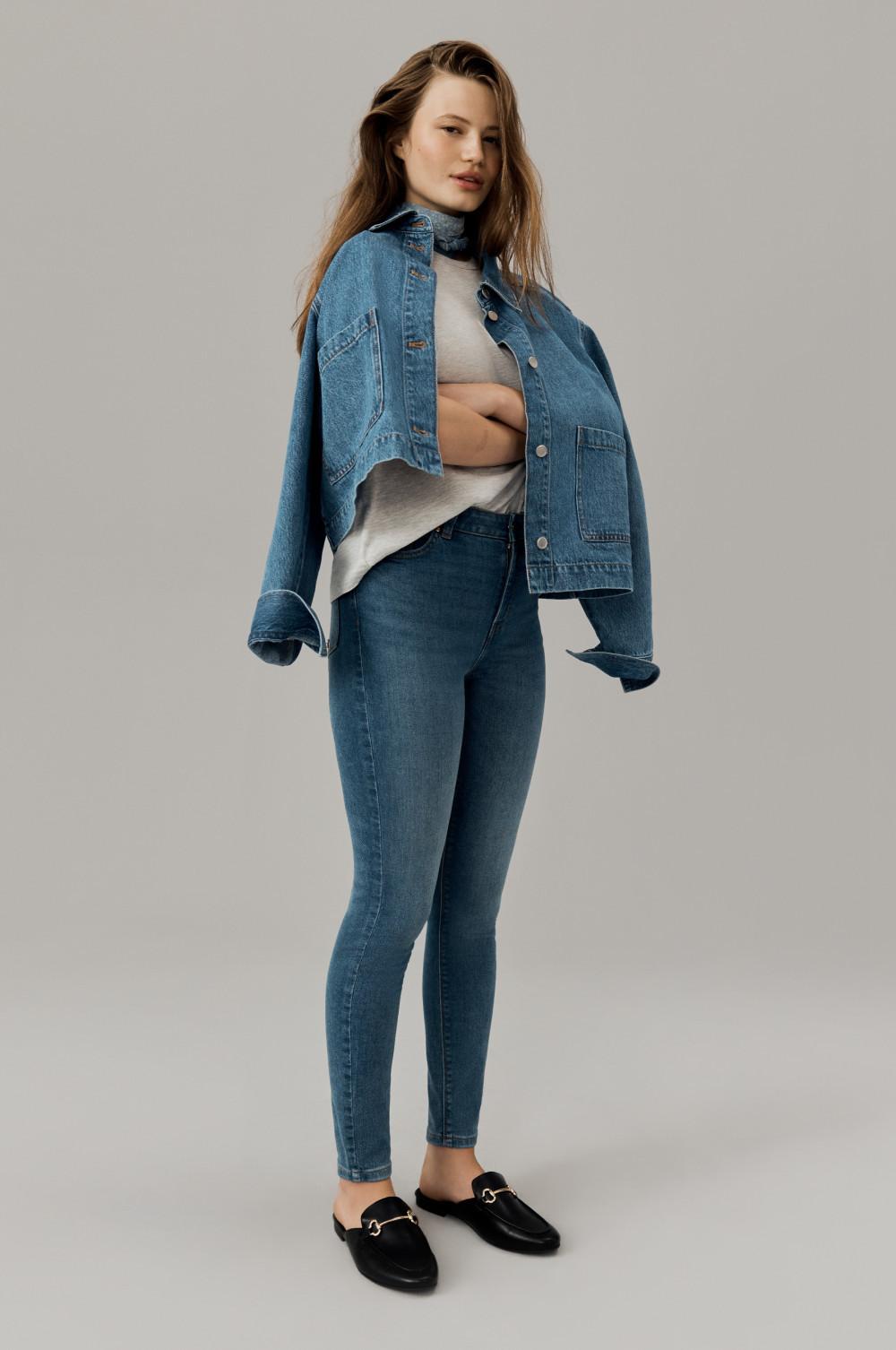 Person wearing denim outfit with oversized jacket, skinny jeans, white top and black loafers.