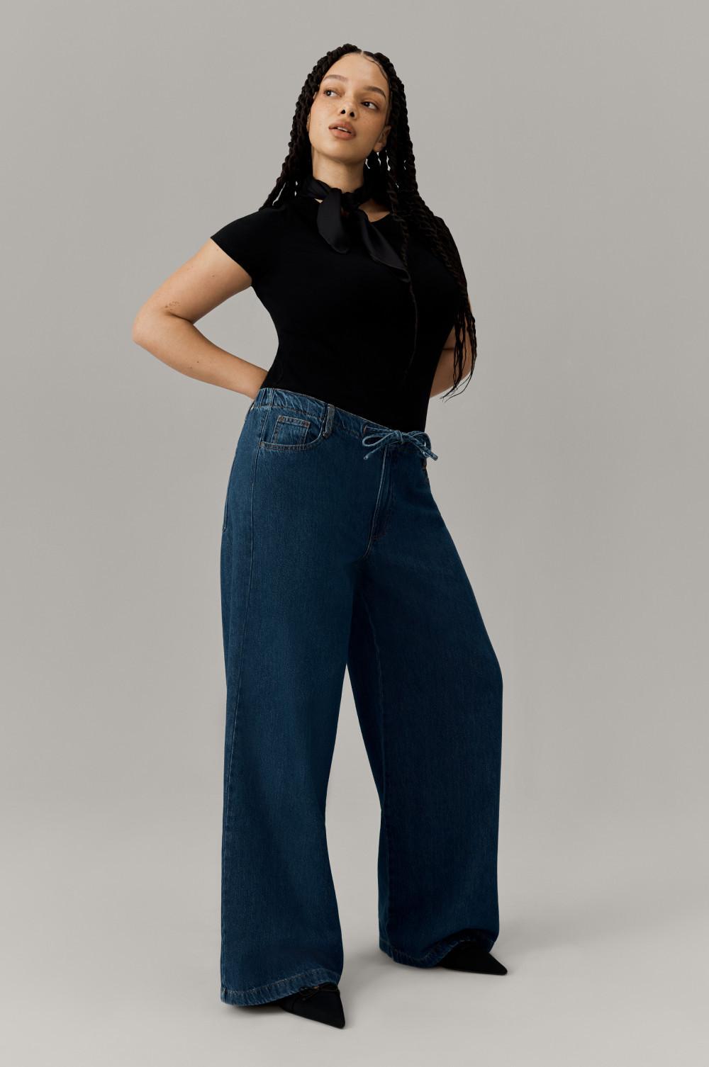 Person wearing black short-sleeve top with bow detail and wide-leg blue denim jeans against neutral background.