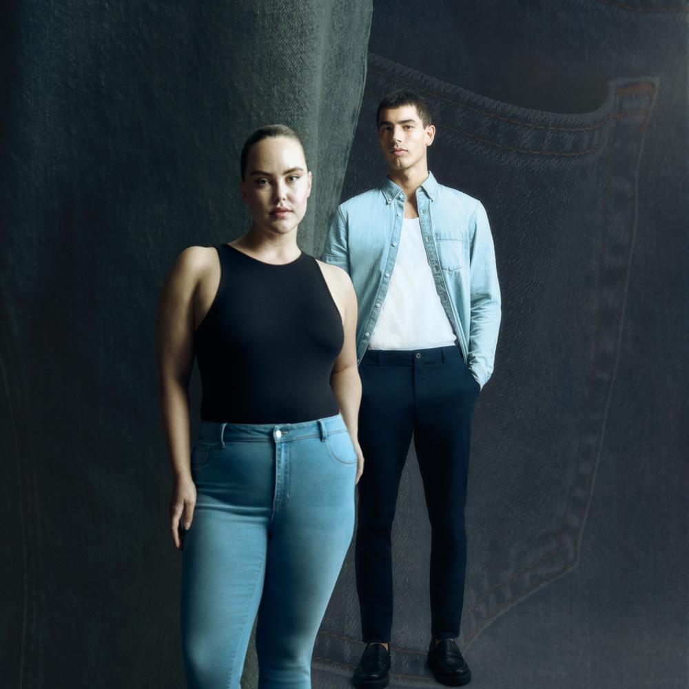 Zwei Models in Freizeitkleidung, darunter eine helle Jeans, ein schwarzes ärmelloses Oberteil und ein Jeanshemd vor einem dunklen Hintergrund.