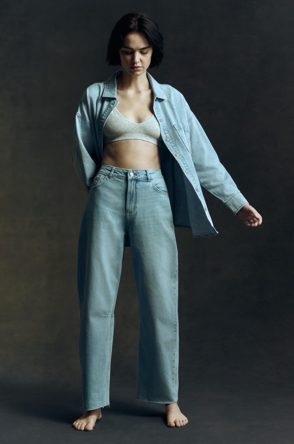 Model in light wash denim shirt, white bralette, blue wash barrel leg jeans