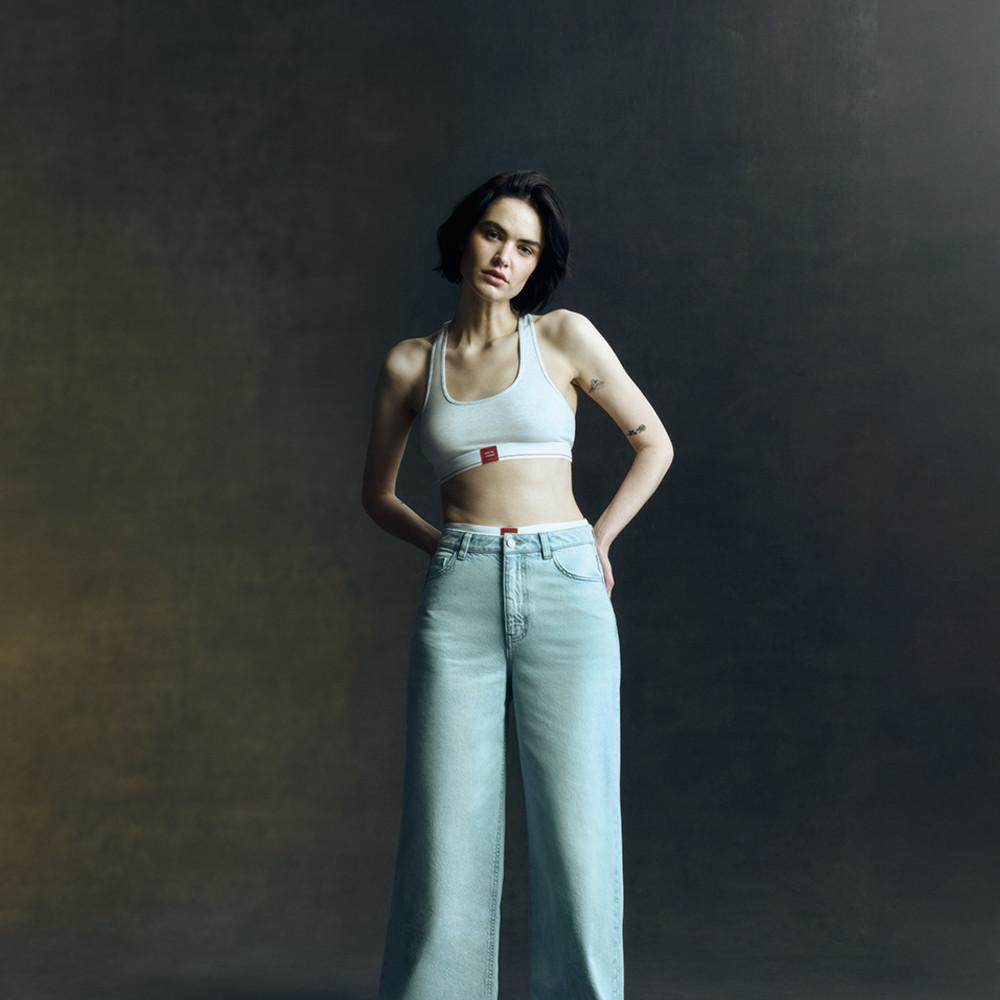 White sports bra, light wash wide leg jeans, barefoot on dark backdrop.