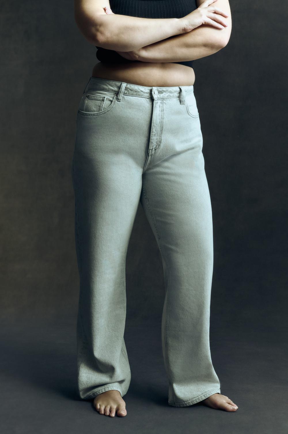 High-Waist-Jeans mit heller Waschung und weitem Bein, hier gezeigt an einem Model mit schwarzem bauchfreien Top und barfuß.