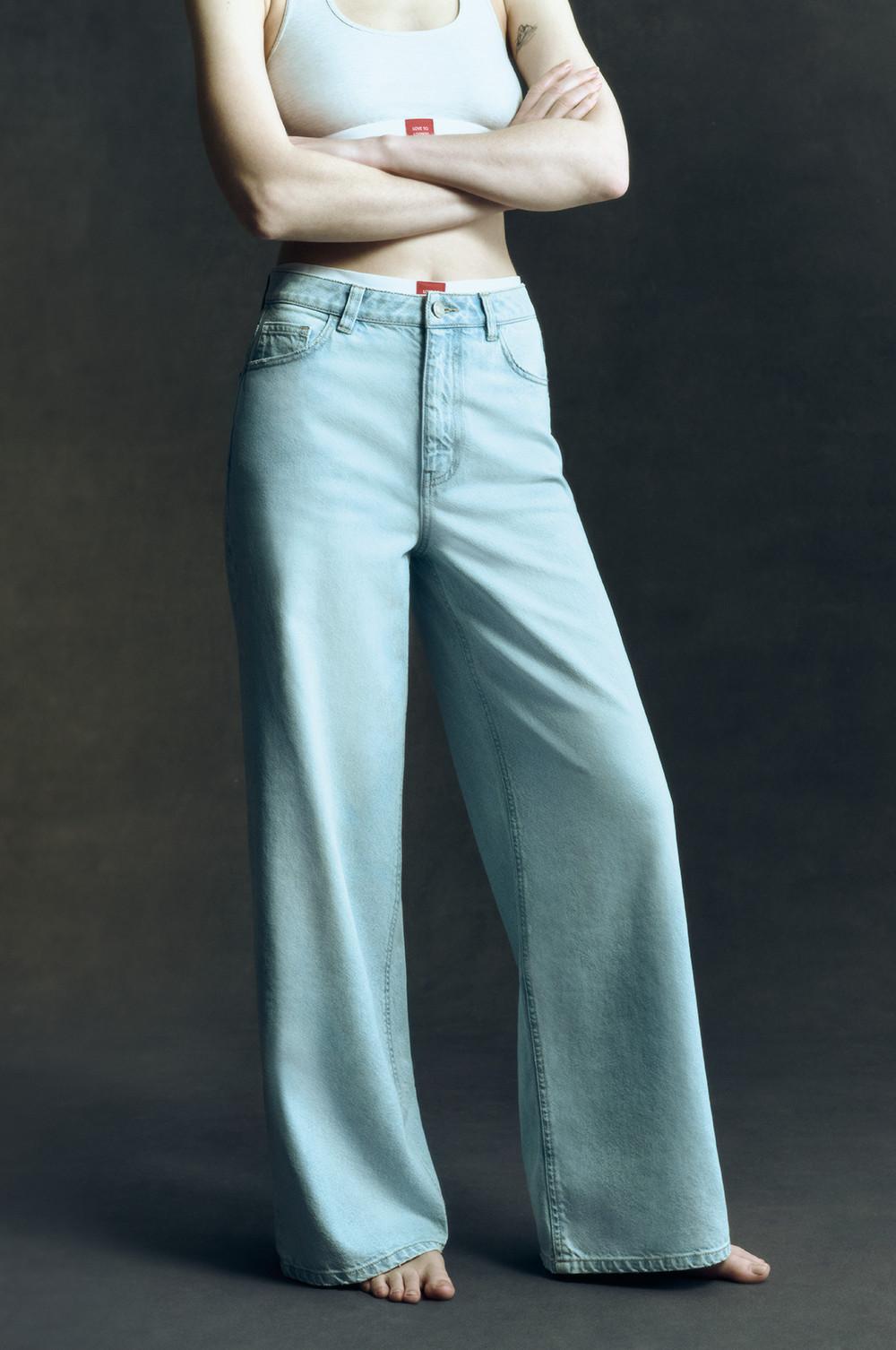 Model in hellblauer Jeans mit weitem Bein und weißem bauchfreiem Top.