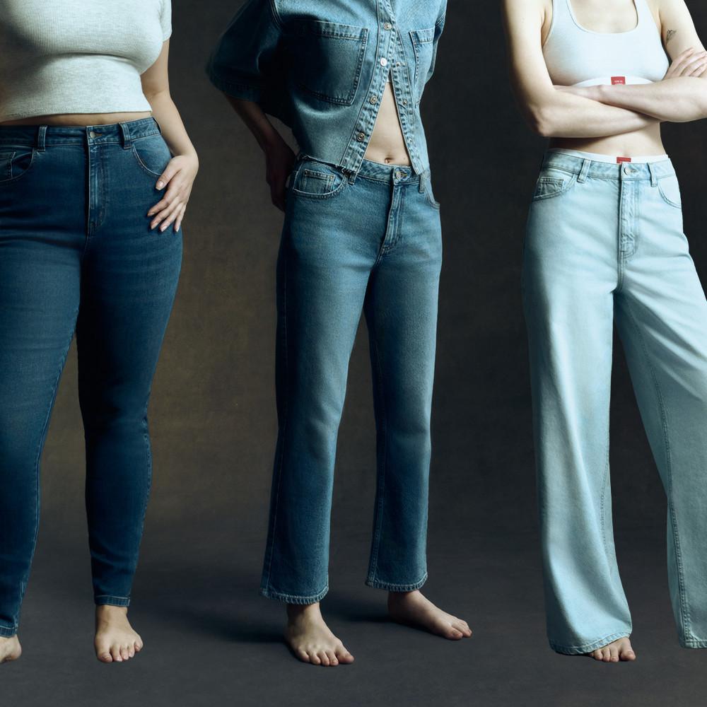 Drei Damen in Jeans – eine in einem bauchfreien Top, eine andere in einer Jeansjacke und die dritte in einem Tanktop.