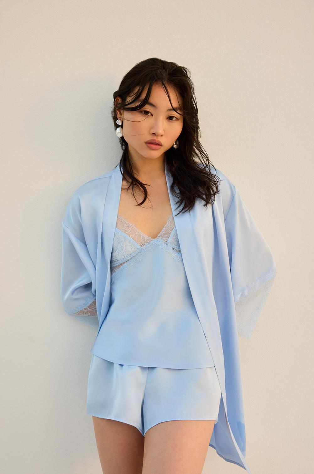 Light blue silk pyjama set with lace trim camisole, shorts and matching robe. Pearl earrings complete the look.