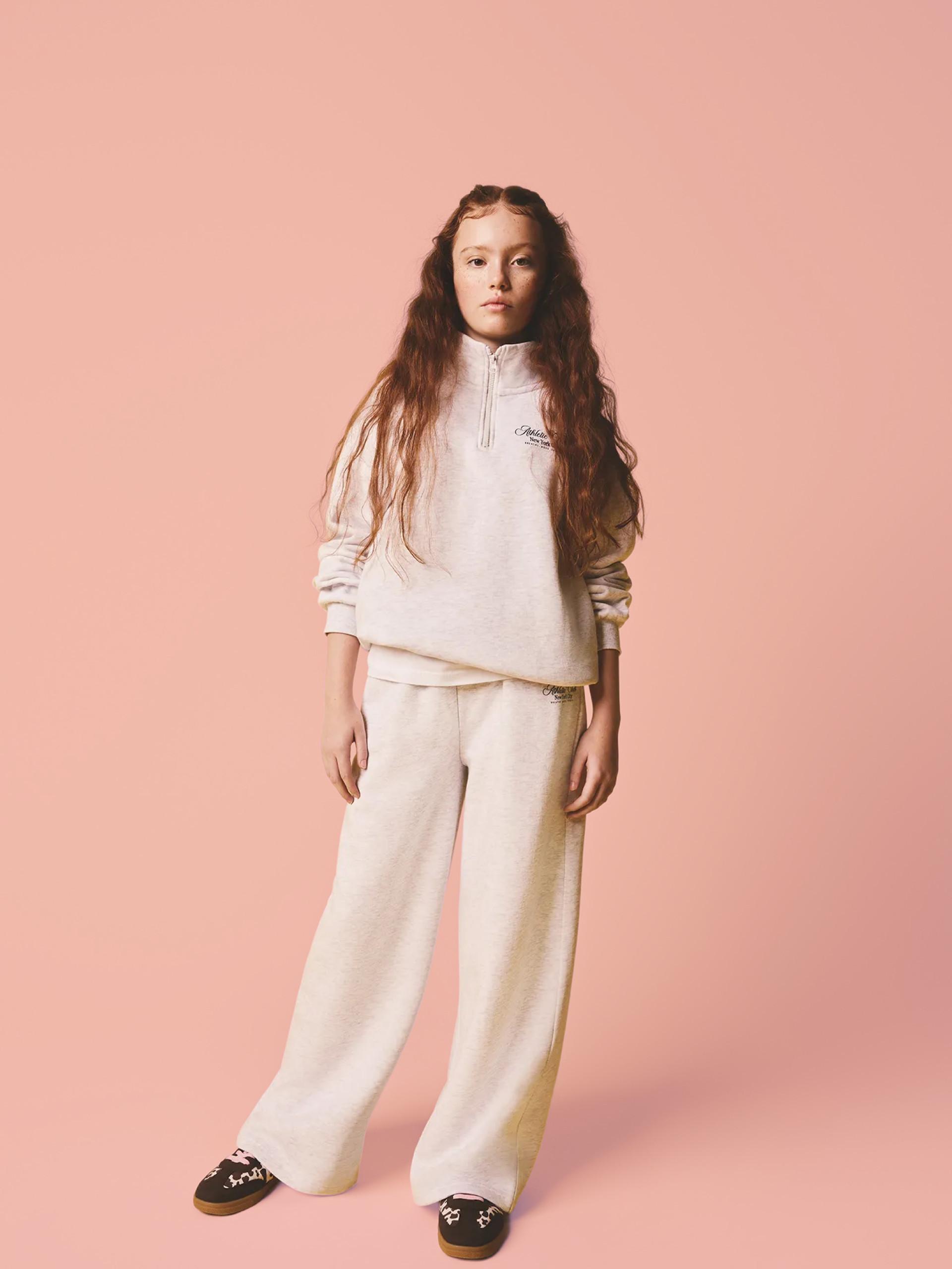 Child wearing cream quarter-zip sweatshirt with matching wide-leg trousers against pink background.