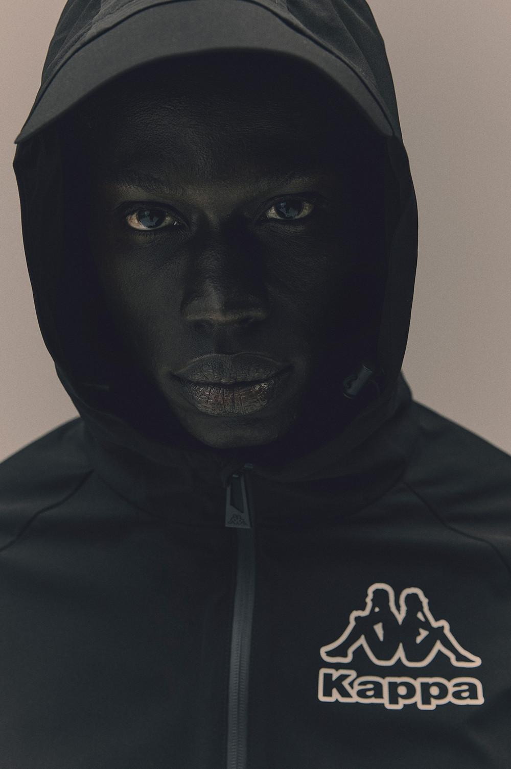 Nahaufnahme eines Models in schwarzer Kapuzenjacke mit weißem Kappa-Logo