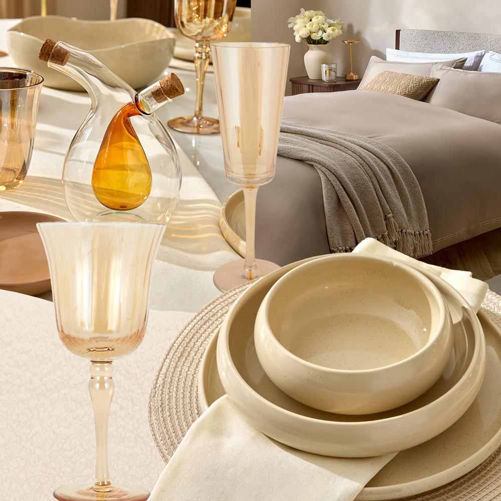 Elegante Tischdeko mit Sektgläsern, cremefarbenen Keramikschüsseln und einer dekorativen Ölflasche neben einem gemachten Bett mit Blumen.