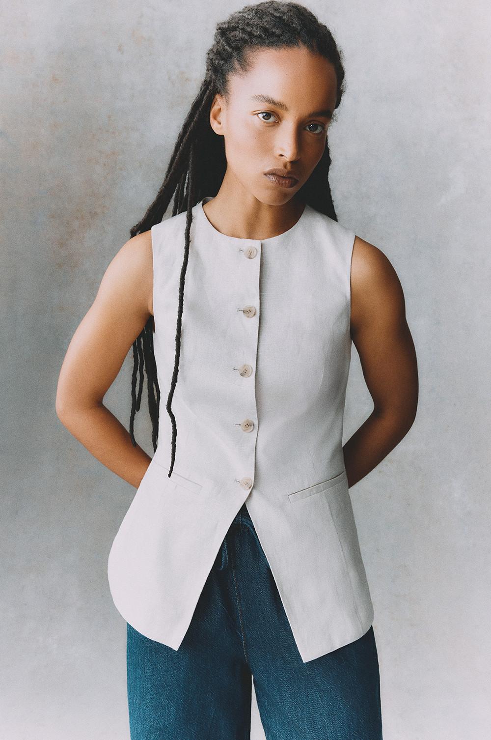 Model wearing sleeveless white button-up top paired with blue jeans.