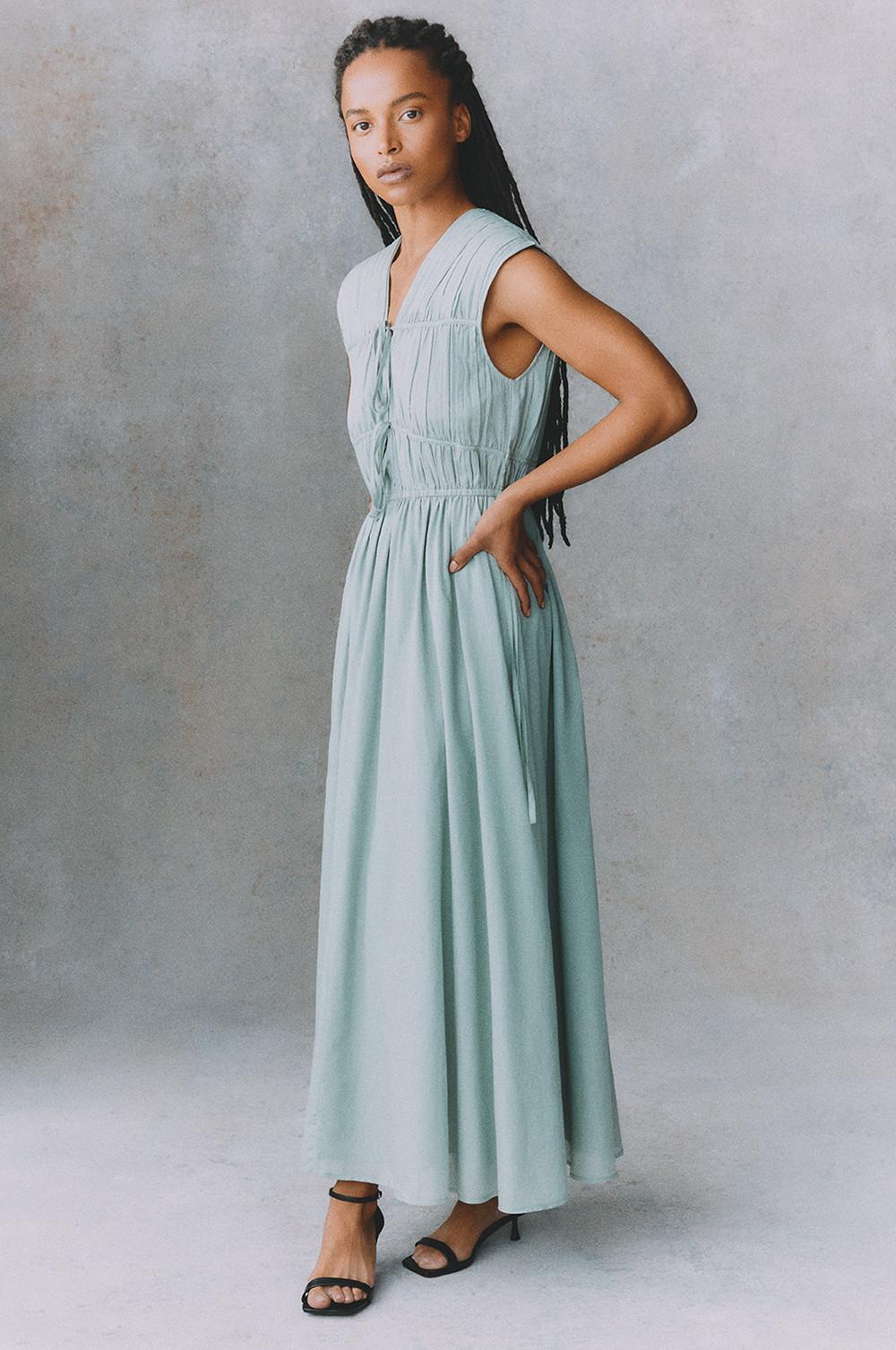Baby blue sleeveless maxi dress with gathered waist detail and tie front, paired with black ankle strap sandals.