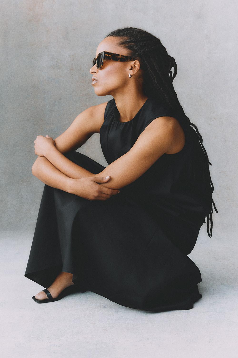 Model wearing sleeveless black top with matching maxi with tortoiseshell sunglasses and black kitten heels in side profile pose.