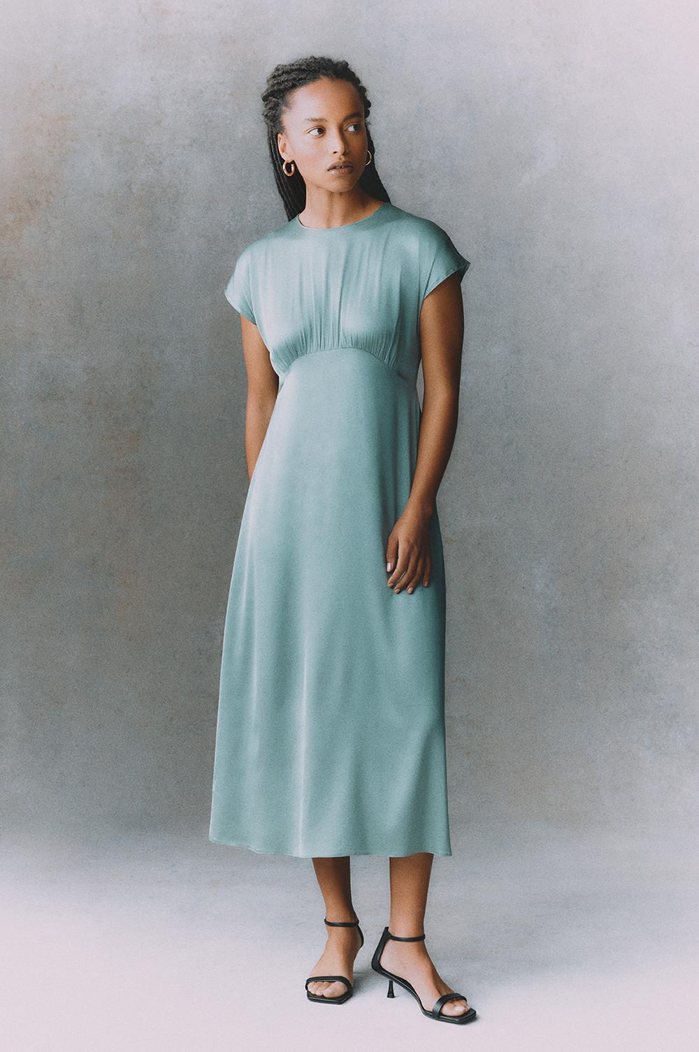 Pastel blue midi dress with gathered waist, cap sleeves and black ankle-strap sandals worn by model in fashion pose.