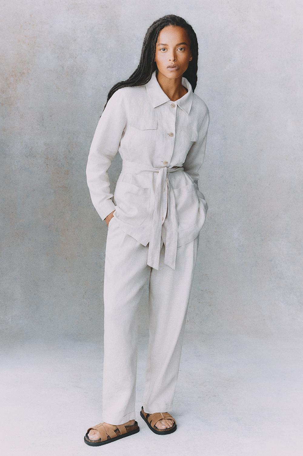 White linen jumpsuit with utility pockets and belt, paired with tan leather sandals.