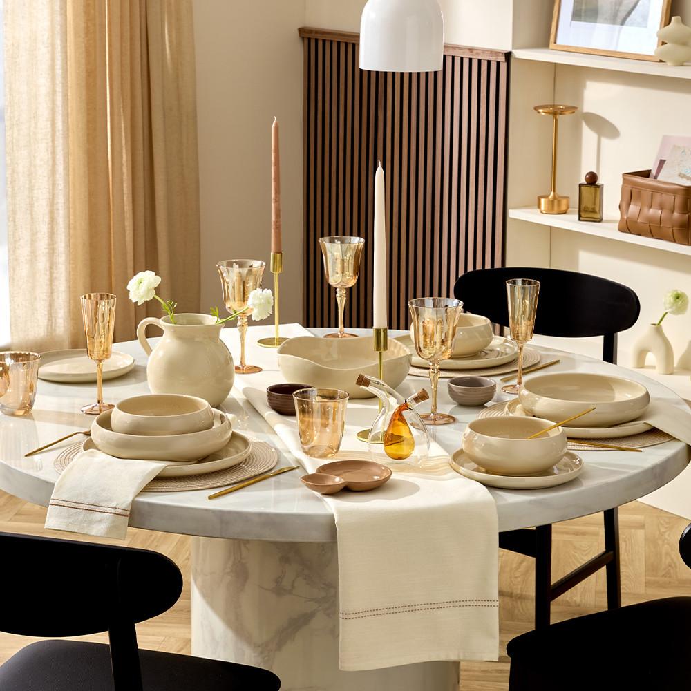 Table decorated with cream plates and bowls, gold tone wine glasses and a cream table runner